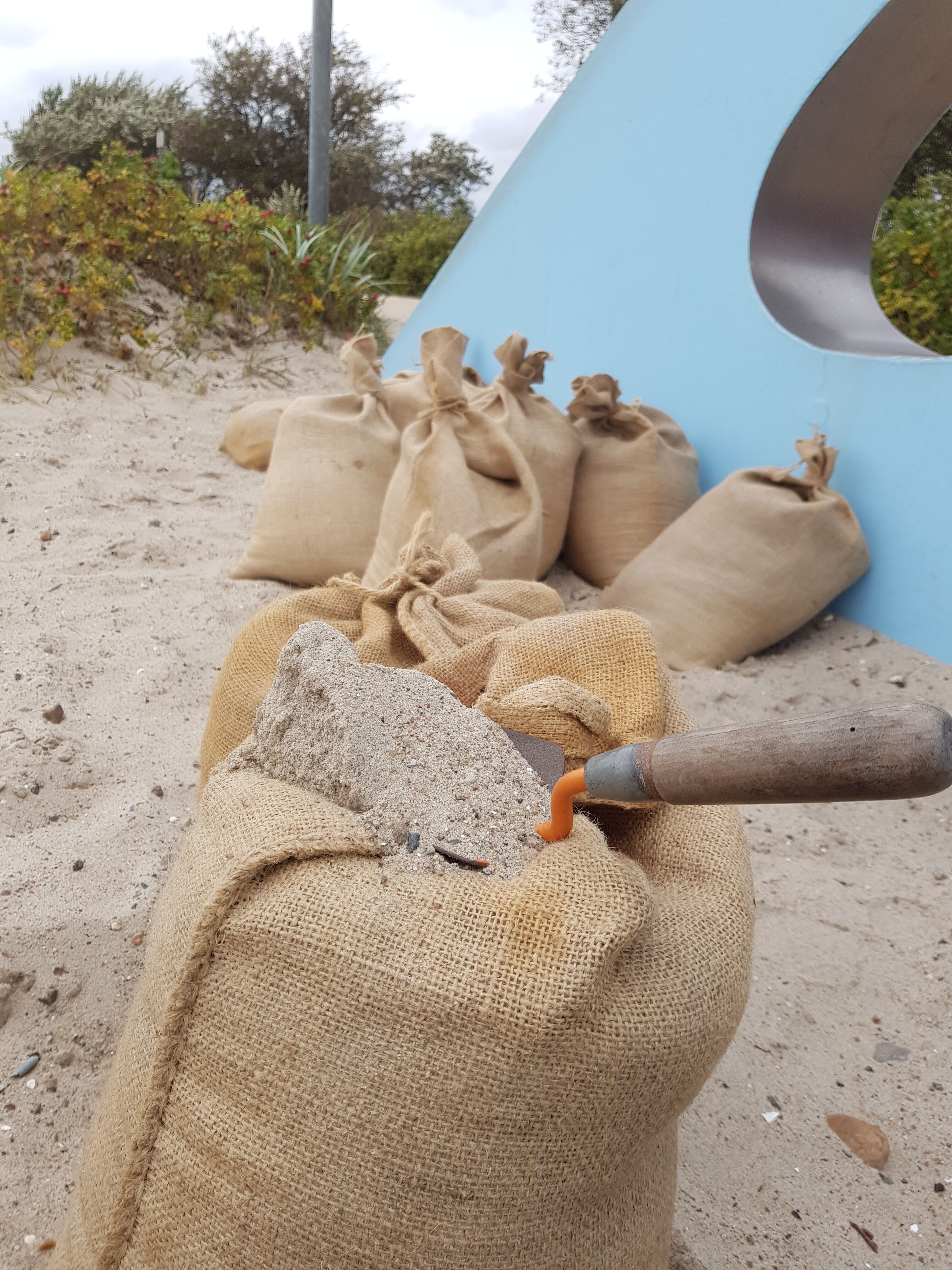 Gefüllter Sandsack mit kleiner Schaufel am Strand von Kellenhusen